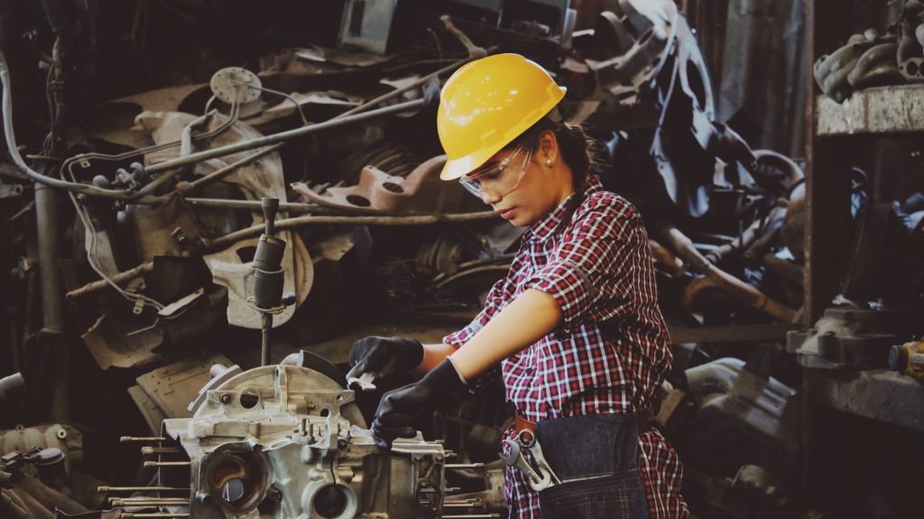 Woman wearing yellow hard hat and protection googles working with metal